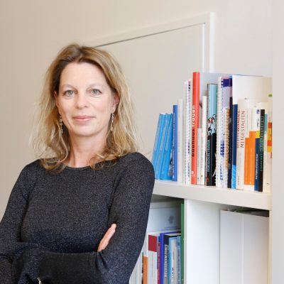 Dr. Andrea Taubenbeok stehend vor einem Bücherregal